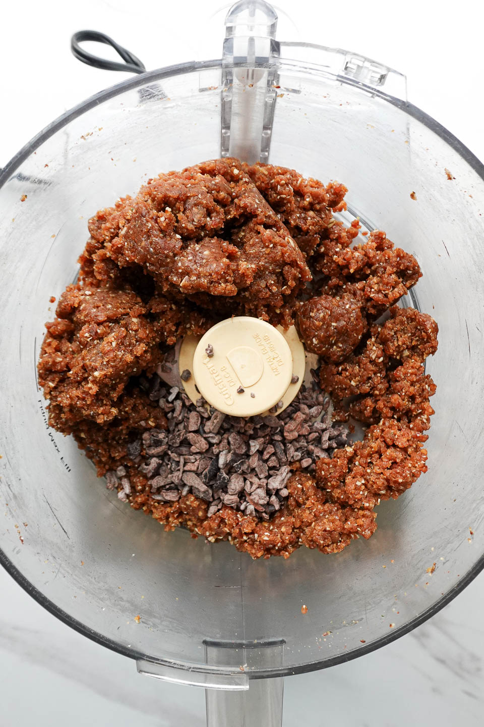 Adding cacao nibs to peanut butter date mixture in food processor and pulsing until combined