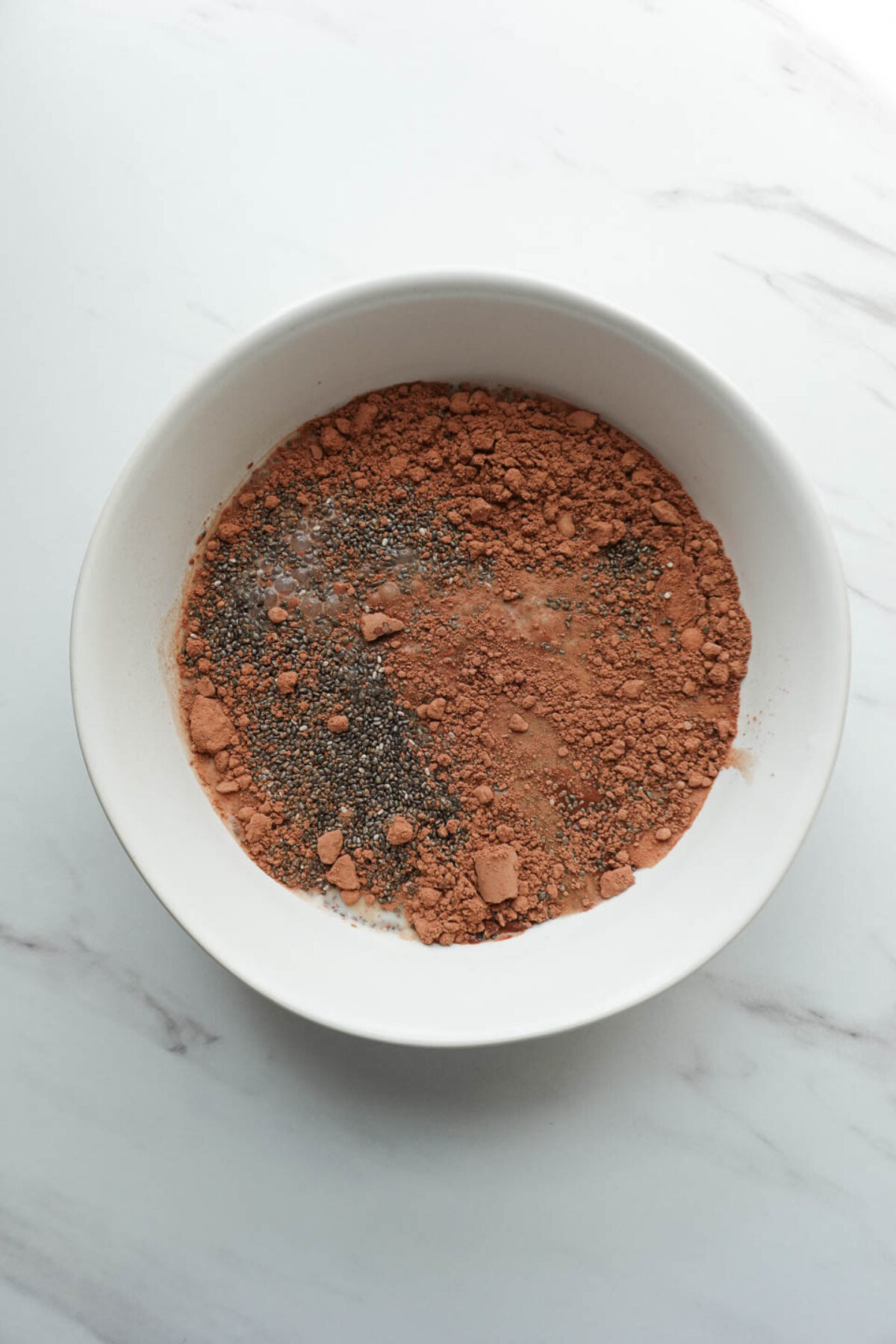 Mixing chia seeds, cocoa powder, maple syrup, vanilla extract, and non-dairy milk to make chocolate chia pudding layer
