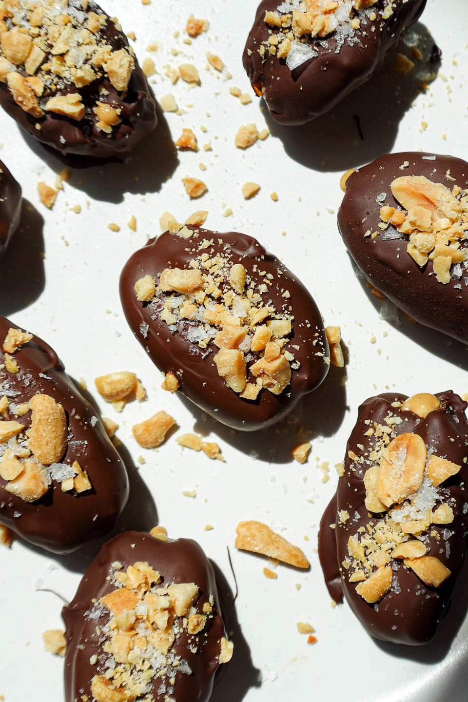 Overhead shot of Snickers Stuffed Dates on a parchment-lined tray, dipped in chocolate and sprinkled with chopped peanuts.