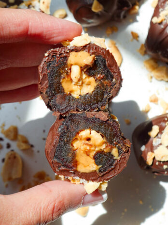 Hand holding a Snickers Stuffed Date with a bite taken out to show the caramel-like texture of the Medjool date.