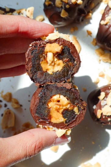 Hand holding a Snickers Stuffed Date with a bite taken out to show the caramel-like texture of the Medjool date.