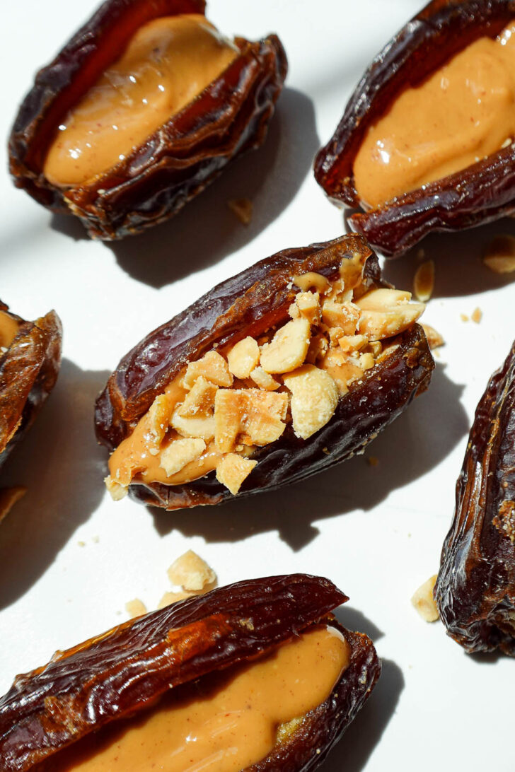 Process shot of dates being stuffed with peanut butter and peanuts before dipping in melted chocolate.