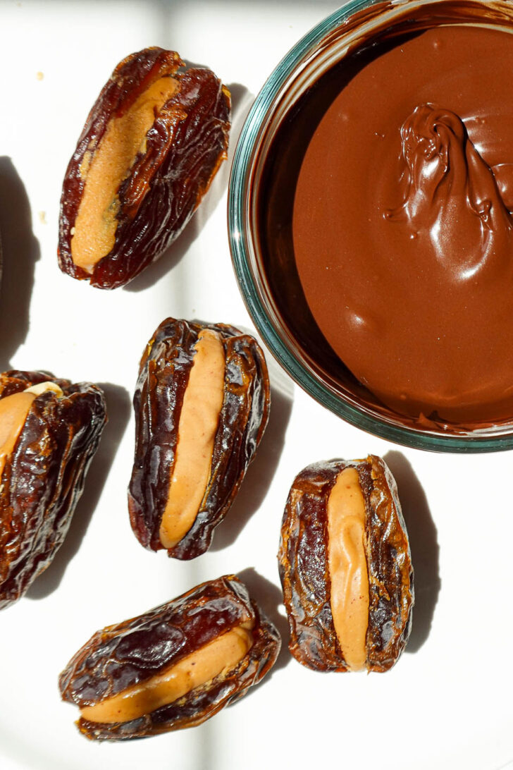 Process shot of dates being stuffed with peanut butter and peanuts before dipping in melted chocolate.