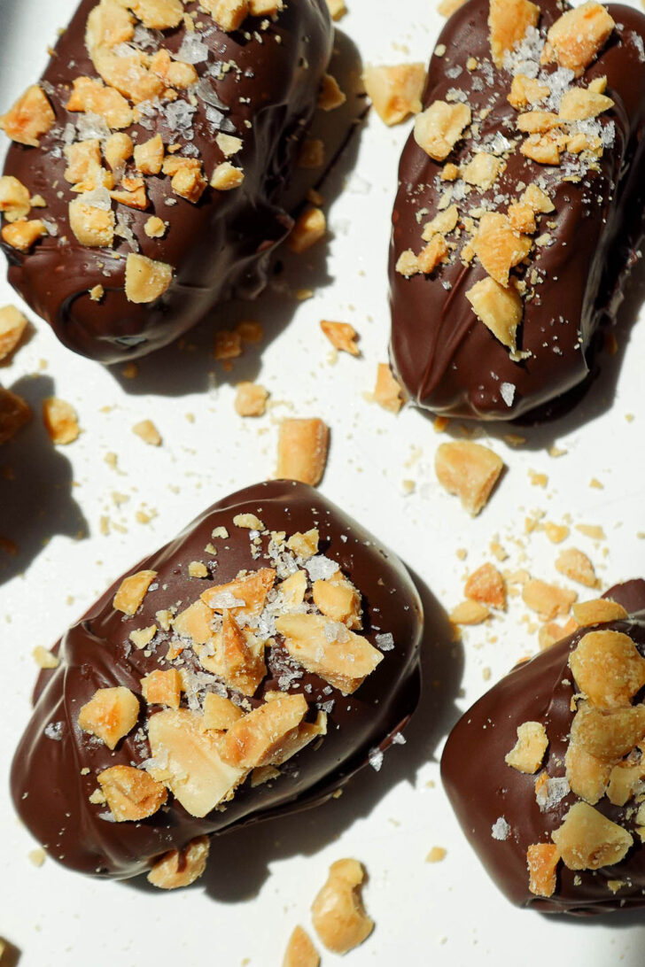 Overhead shot of Snickers Stuffed Dates on a parchment-lined tray, dipped in chocolate and sprinkled with chopped peanuts.