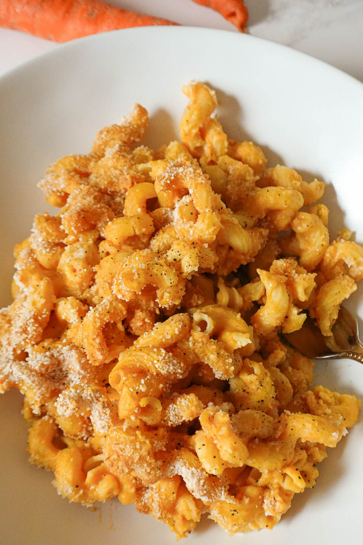 Close-up of creamy vegan mac and cheese made from potatoes and carrots and topped with breadcrumbs for a baked mac and cheese version, served in a white bowl