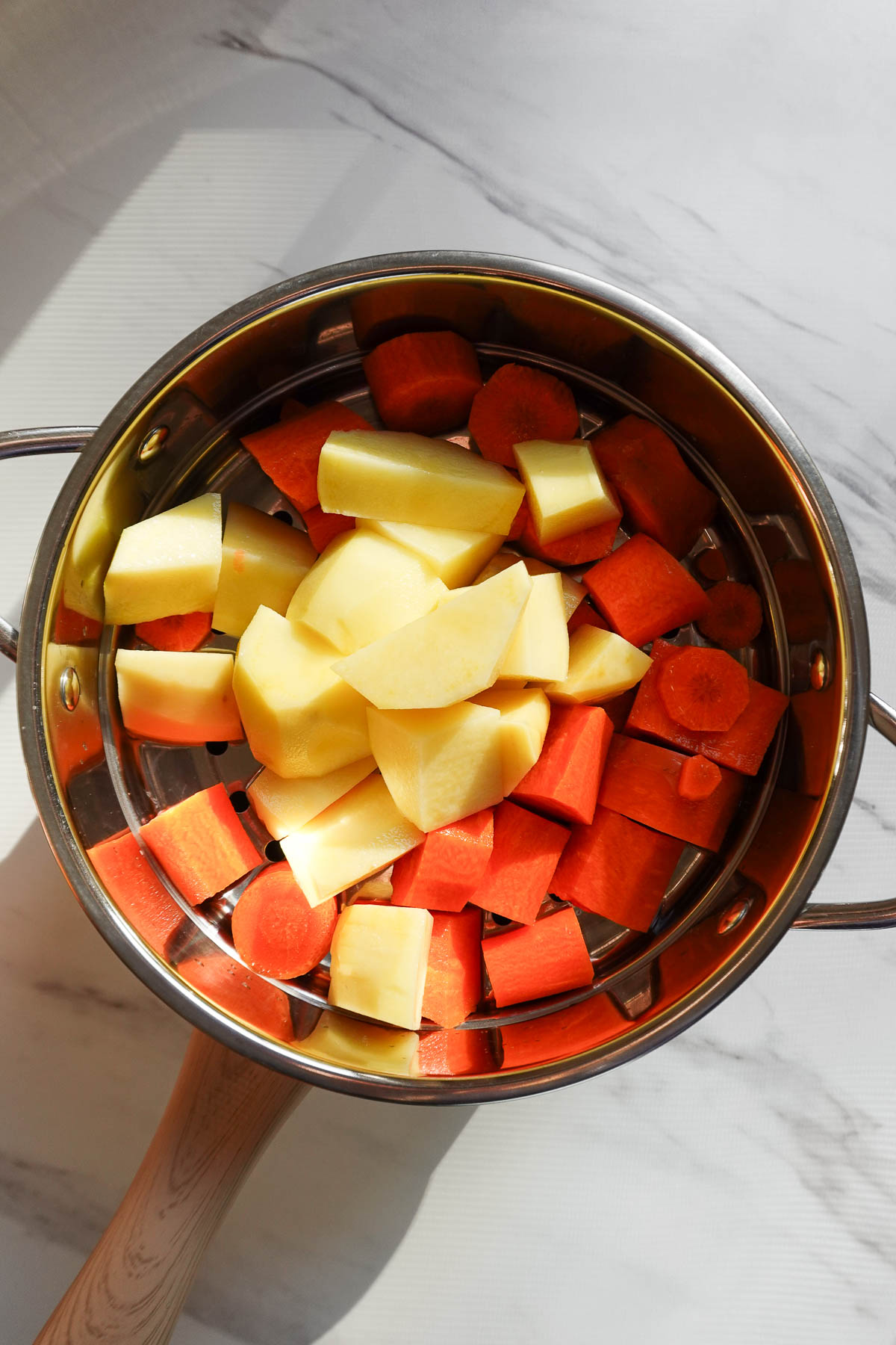 Chopped potatoes and carrots in a steamer basket.