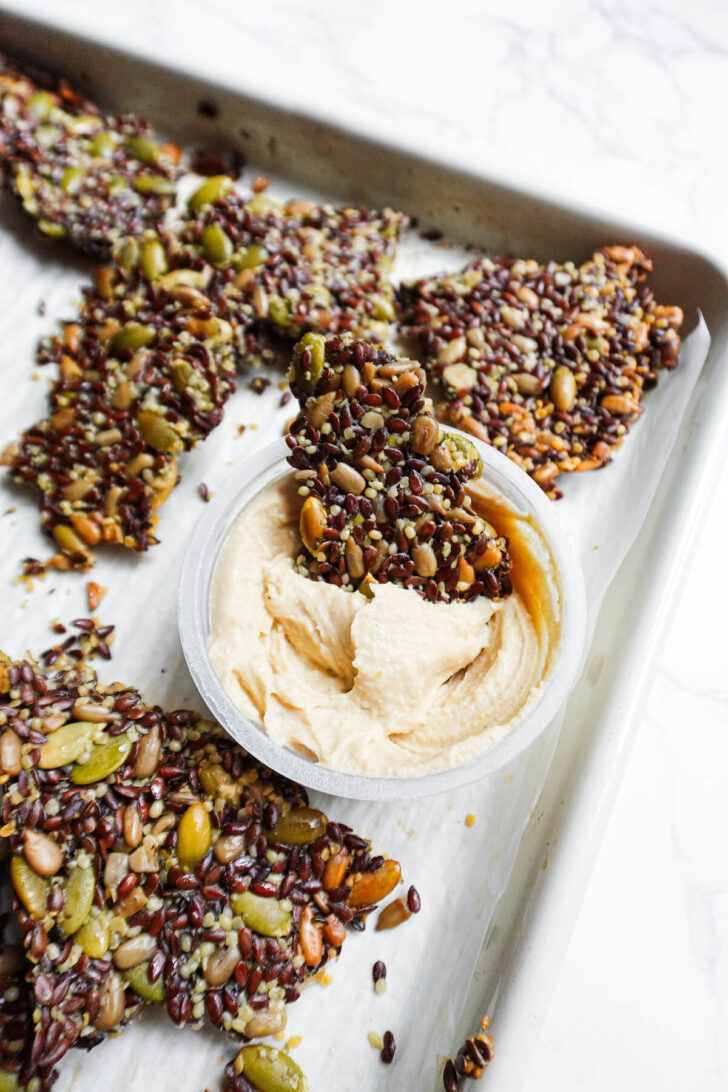 homemade flax seed crackers on a baking sheet with a bowl of hummus