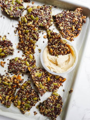 homemade flax seed crackers on a baking sheet with a bowl of hummus