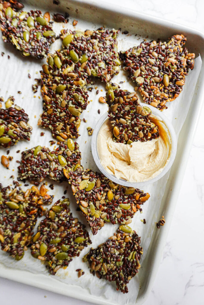 homemade flax seed crackers on a baking sheet with a bowl of hummus