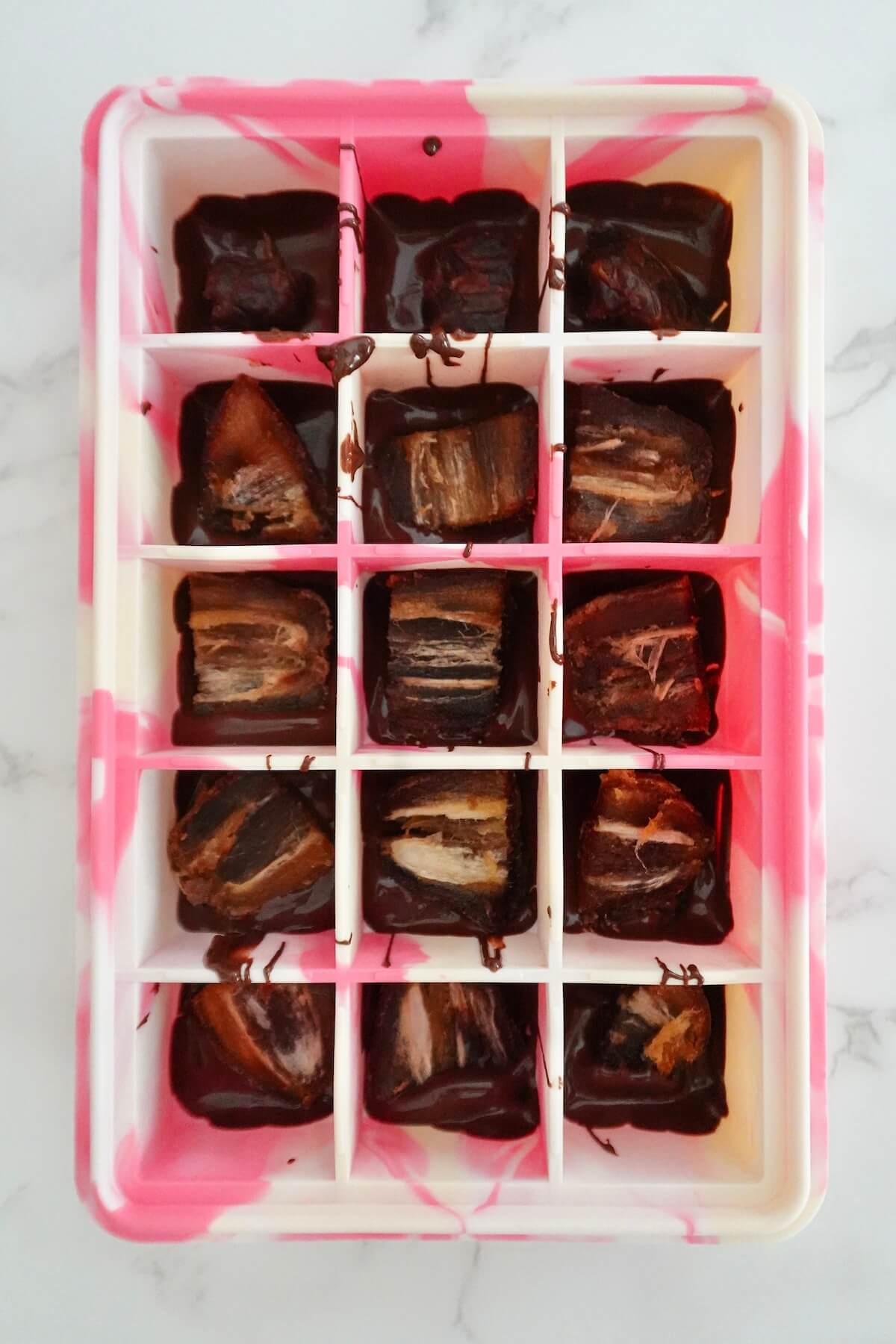A quartered medjool date placed into each chocolate-lined cavity of a silicone mold.