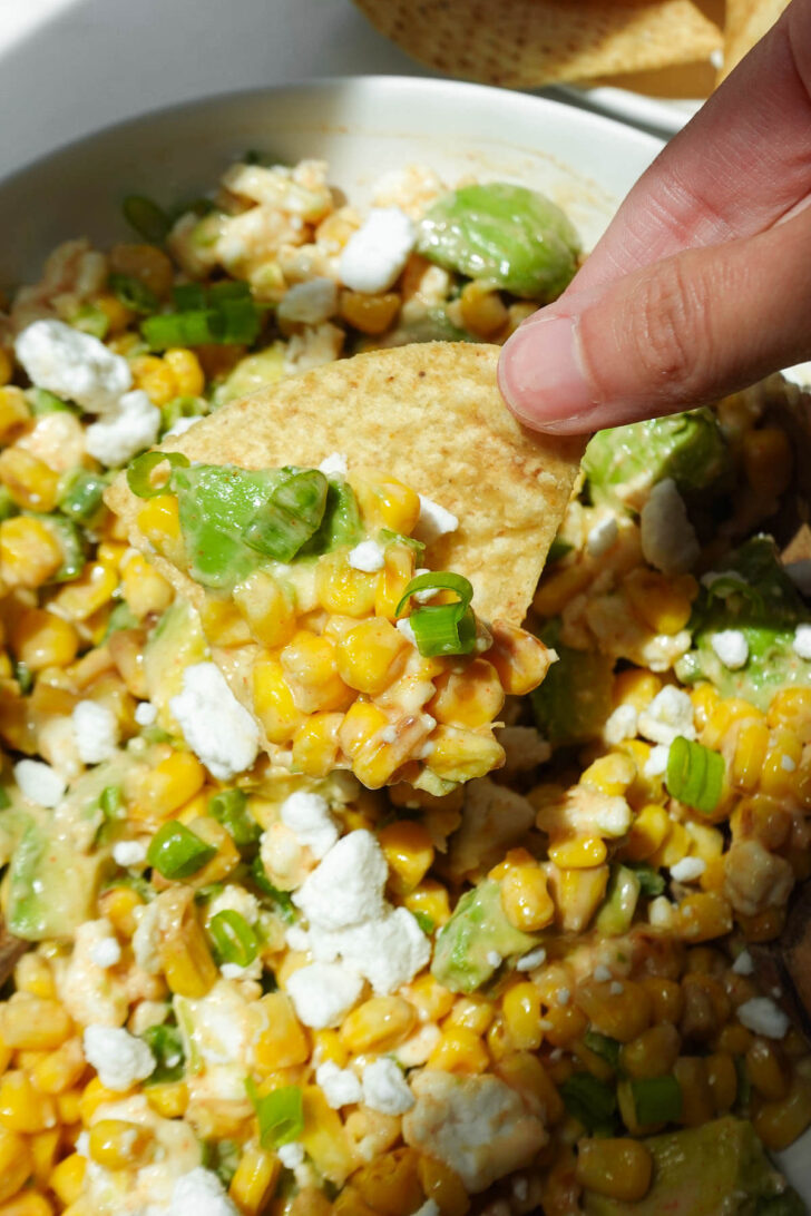 Close-up of vegan elote salad on a tortilla chip with charred corn, avocado, and vegan feta.