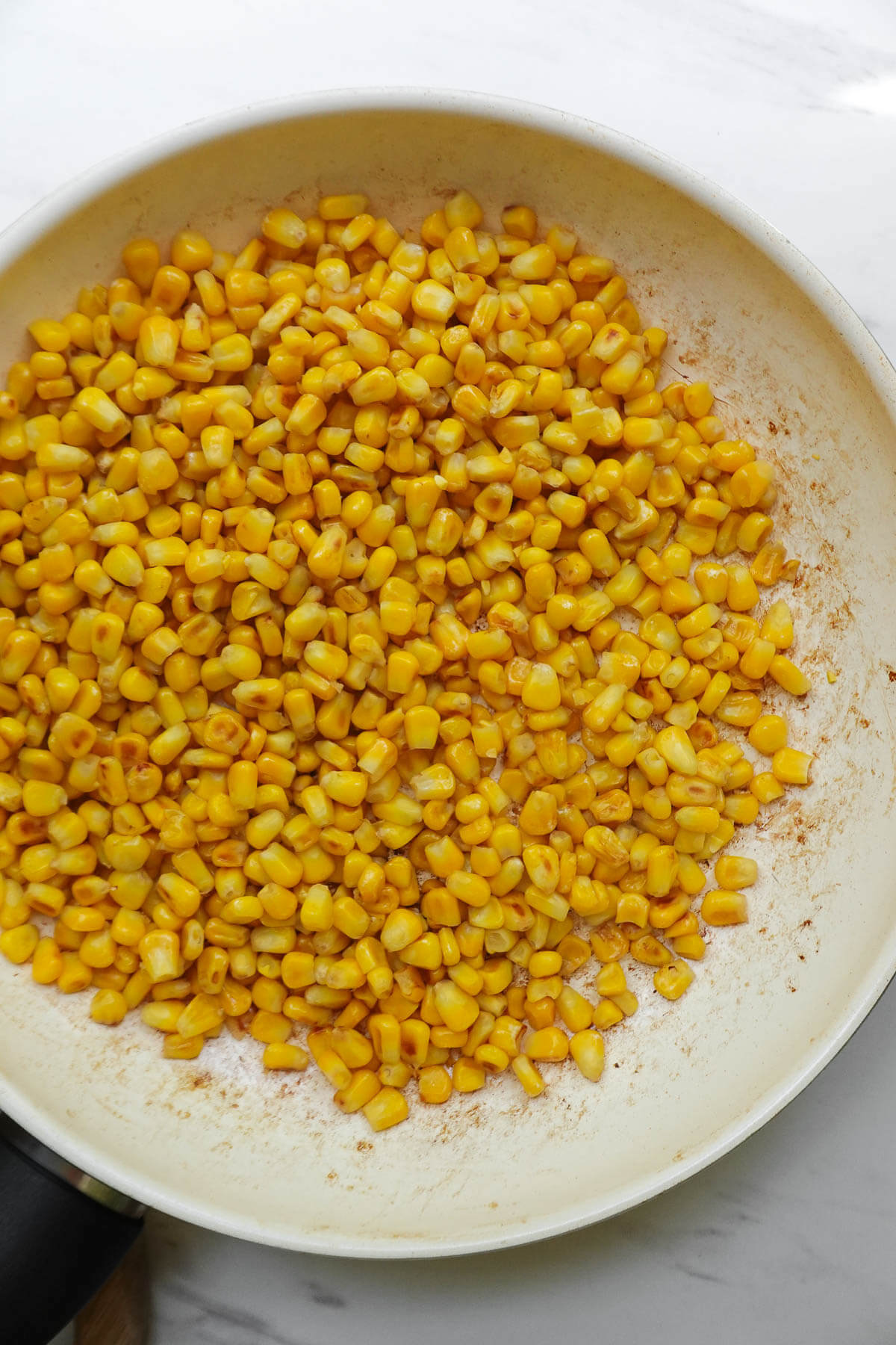 Charred corn kernels cooking in a skillet for Mexican street corn salad.