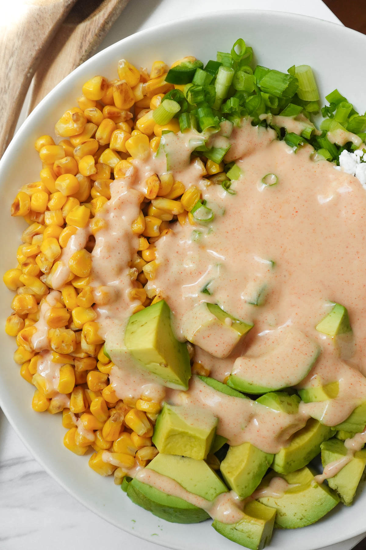 Tossing vegan Mexican street corn salad with creamy dressing.