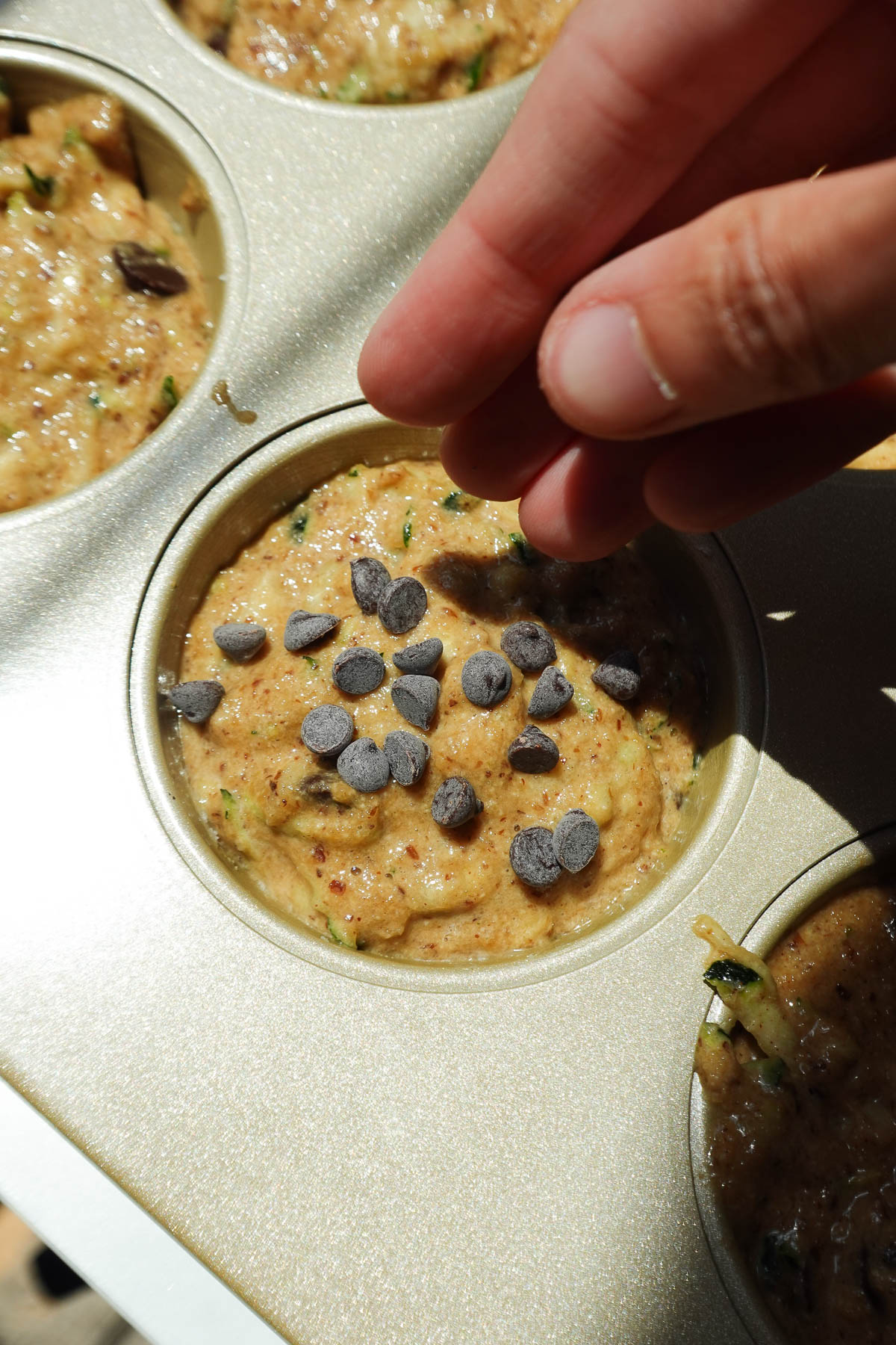 Sprinkling vegan chocolate chips on top of zucchini muffins before baking.