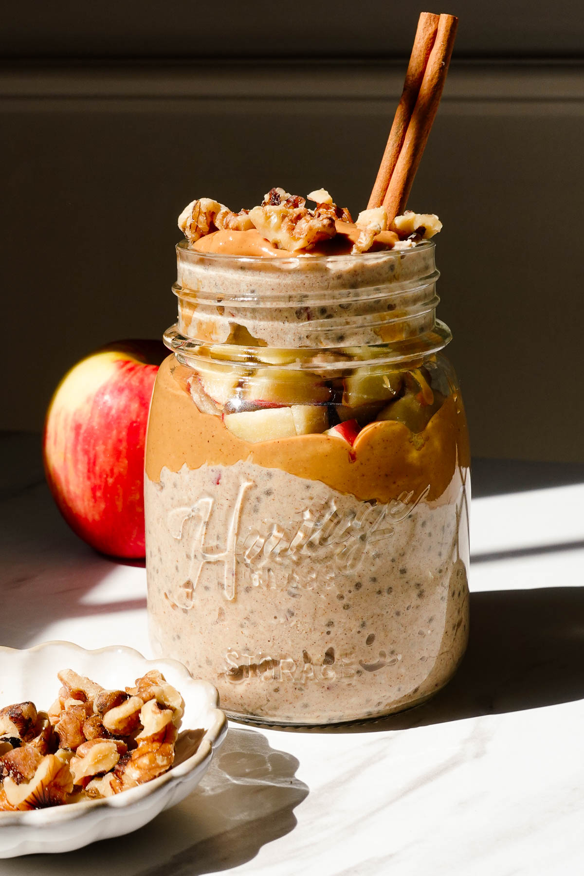 Apple cinnamon overnight oats topped with diced apple, cinnamon, almond butter, and chopped walnuts in a glass jar.