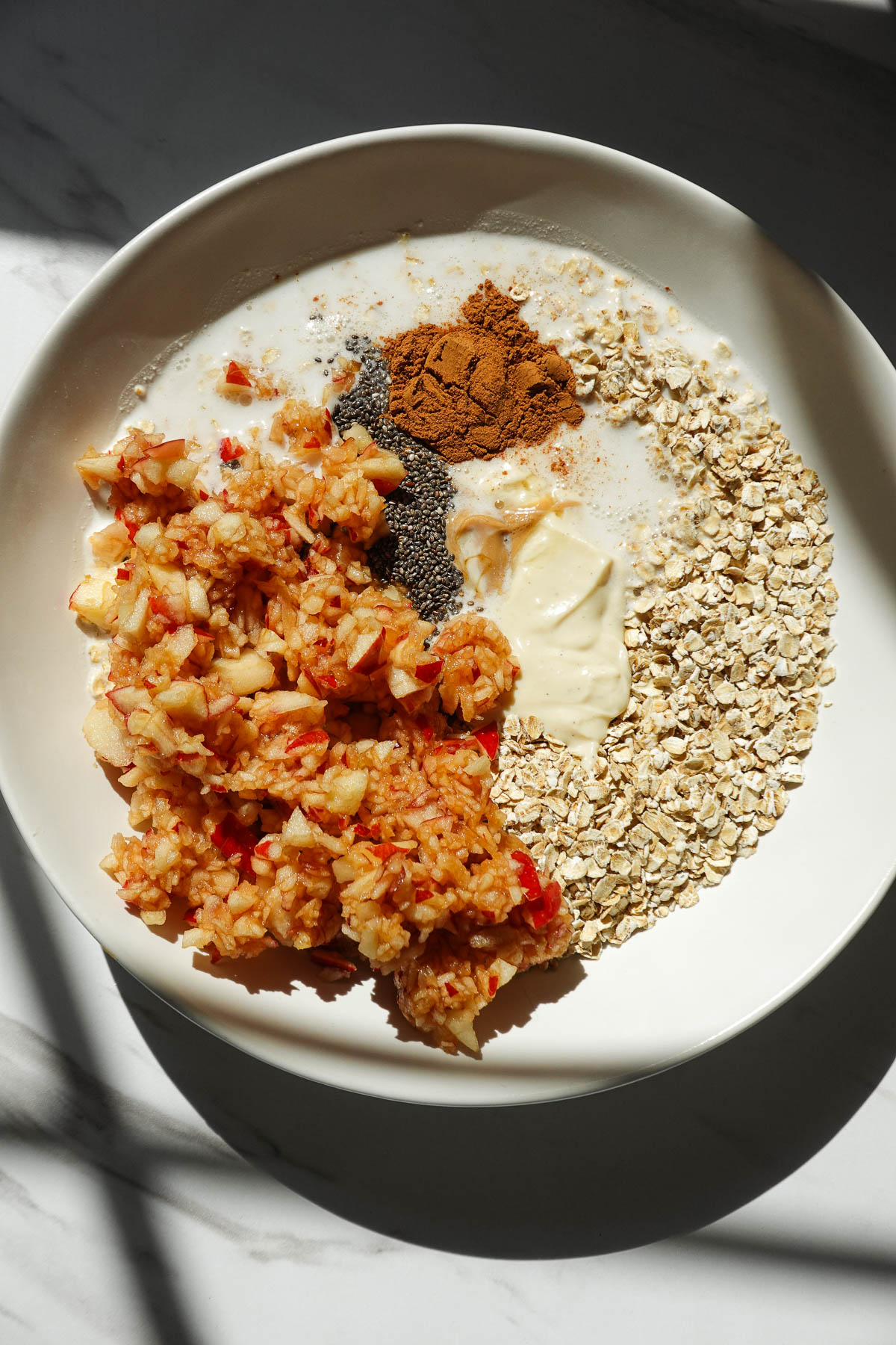 Mixing oats, shredded apple, vegan yogurt, chia seeds, cinnamon, and maple syrup for apple cinnamon overnight oats.