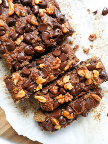 Sliced loaf of vegan banana bread topped with chocolate chips and walnuts.
