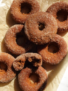 Freshly baked vegan and gluten-free apple cider donuts with cinnamon sugar coating on parchment paper.