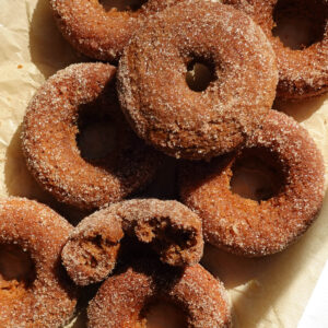 Freshly baked vegan and gluten-free apple cider donuts with cinnamon sugar coating on parchment paper.