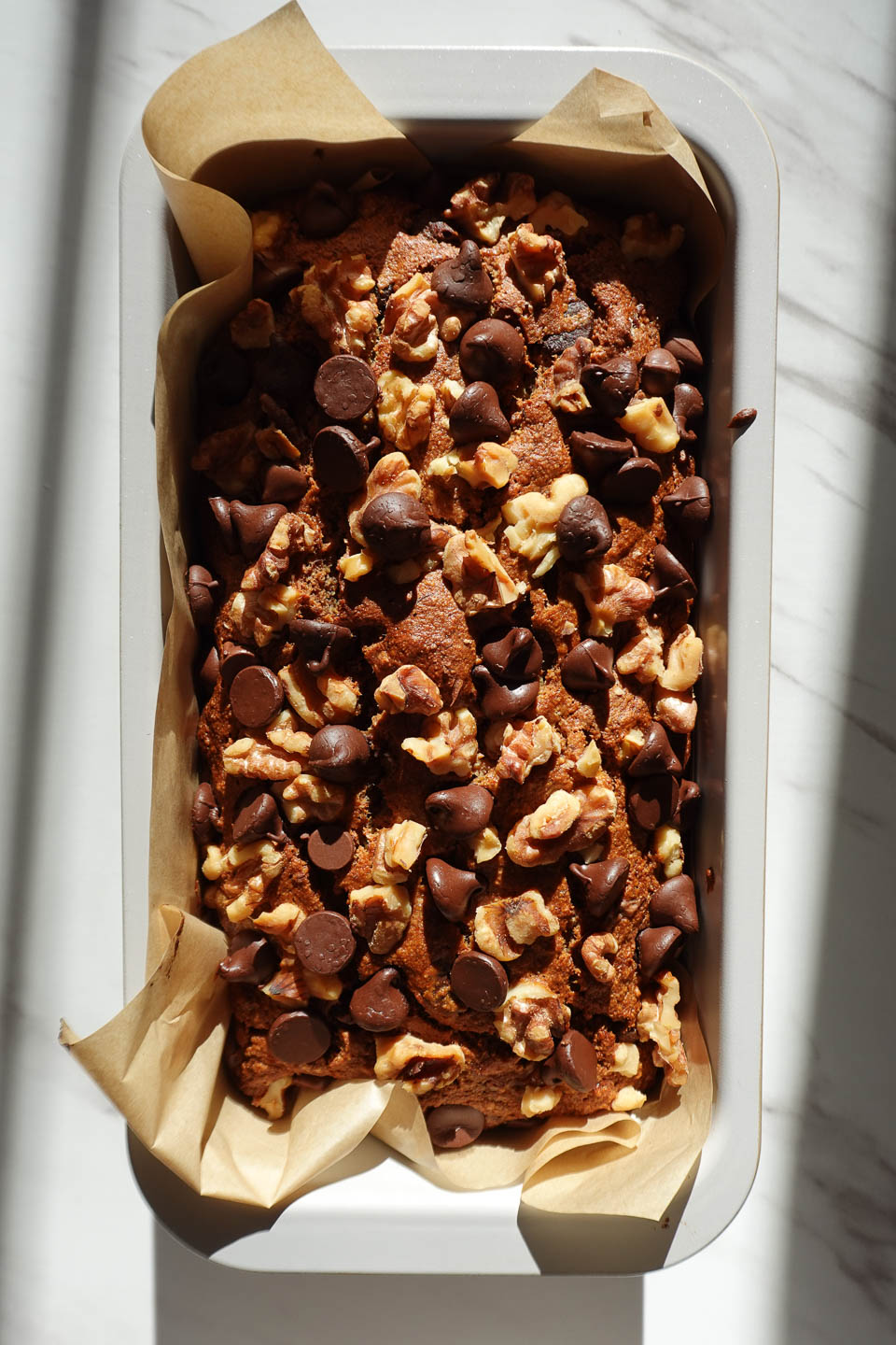 golden baked banana bread after coming out of the oven topped with chopped walnuts and chocolate chips