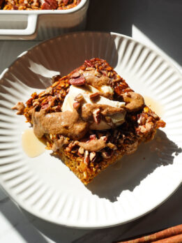 A slice of pumpkin baked oatmeal topped with vegan yogurt and a drizzle of maple syrup and almond butter.