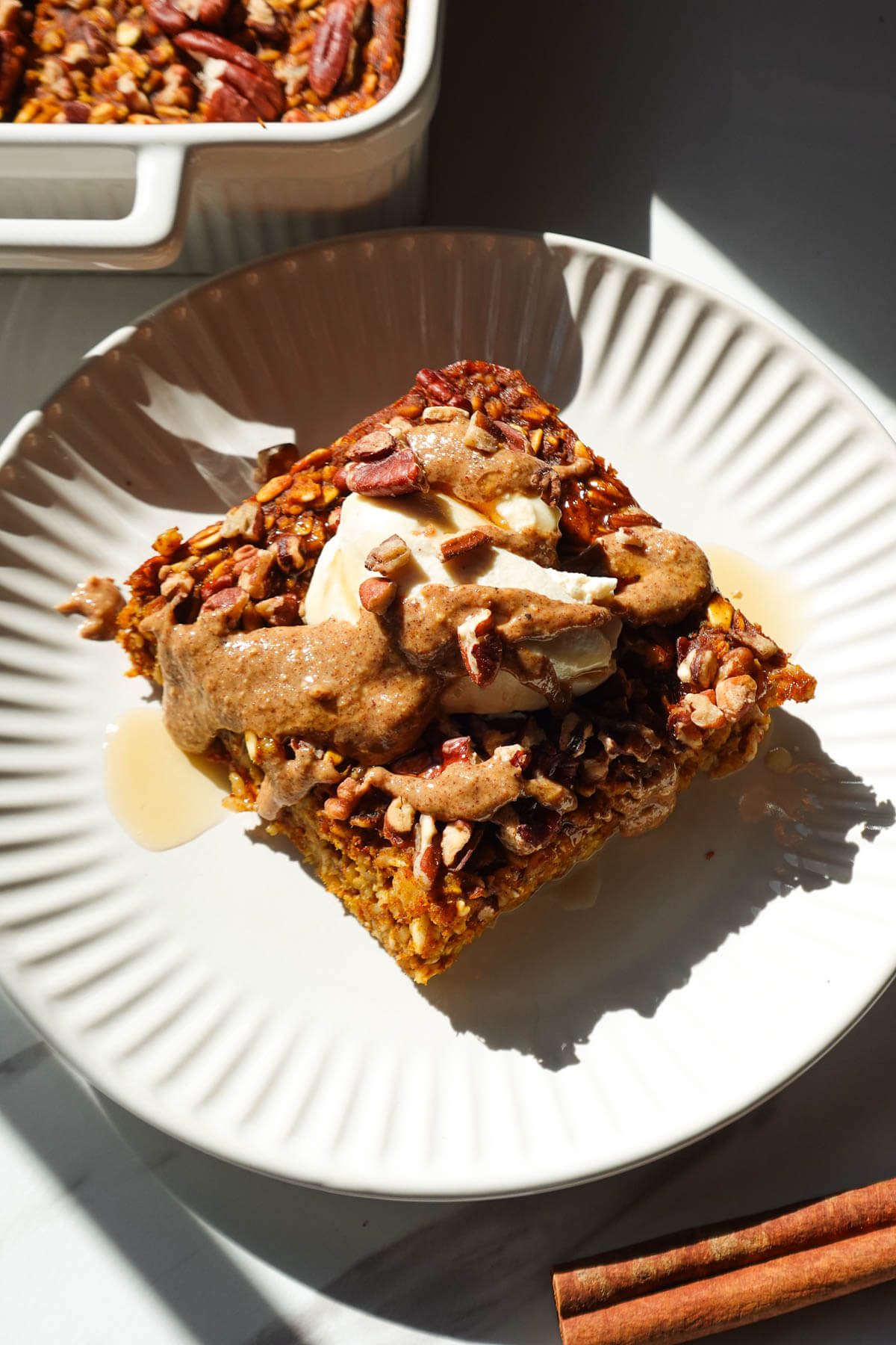 A slice of pumpkin baked oatmeal topped with vegan yogurt and a drizzle of maple syrup and almond butter.