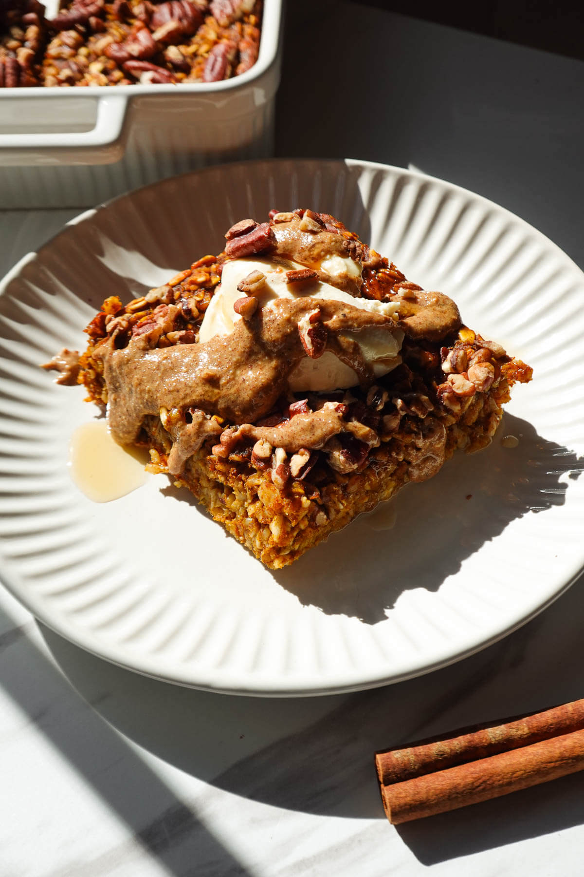 A thick slice of vegan pumpkin baked oatmeal topped with vegan yogurt, almond butter, and maple syrup.