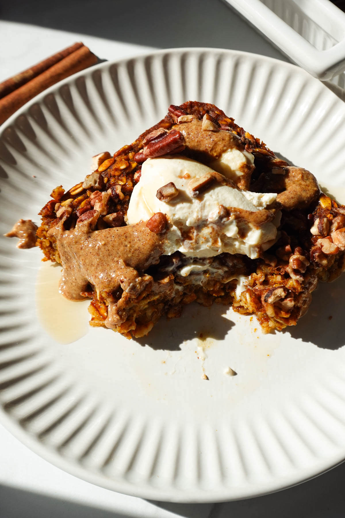 A thick slice of vegan pumpkin baked oatmeal topped with vegan yogurt, almond butter, and maple syrup.
