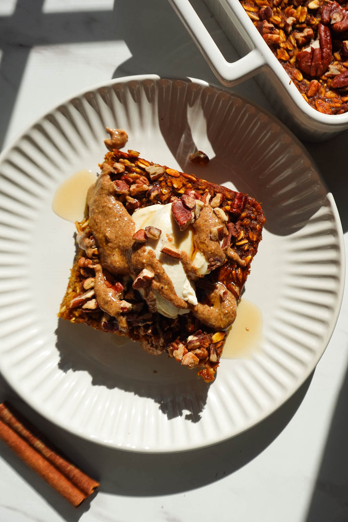 A slice of pumpkin baked oatmeal topped with vegan yogurt and a drizzle of maple syrup and almond butter.