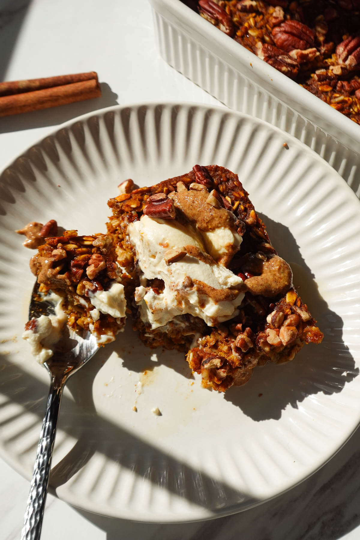 A thick slice of vegan pumpkin baked oatmeal topped with vegan yogurt, almond butter, and maple syrup.