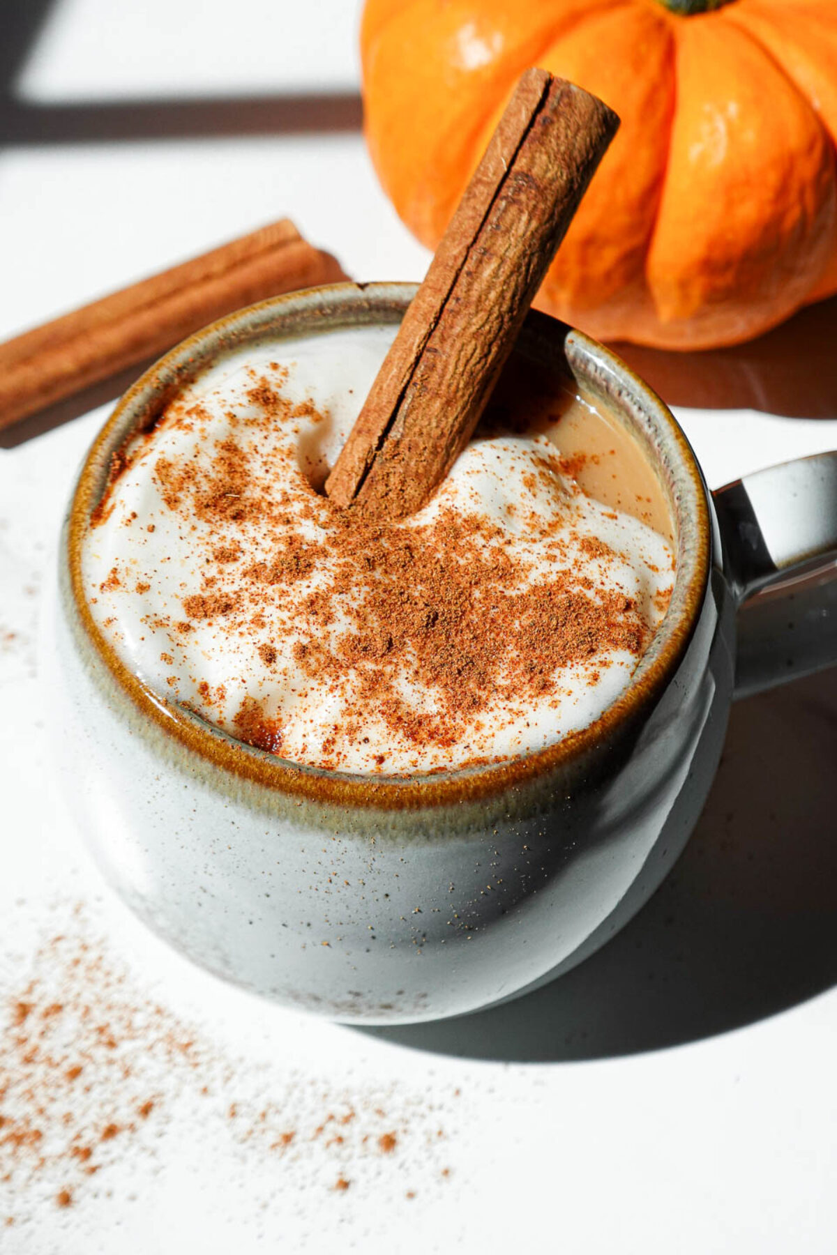 A cozy mug of pumpkin spice chai latte topped with coconut whipped cream, a cinnamon stick, and a sprinkle of pumpkin spice.