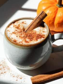 A cozy mug of pumpkin spice chai latte topped with coconut whipped cream, a cinnamon stick, and a sprinkle of pumpkin spice.