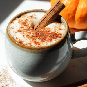 A cozy mug of pumpkin spice chai latte topped with coconut whipped cream, a cinnamon stick, and a sprinkle of pumpkin spice.