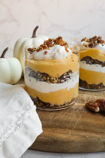 Layered vegan pumpkin cheesecake trifle in a glass jar with pecan-date crumble and coconut whipped cream