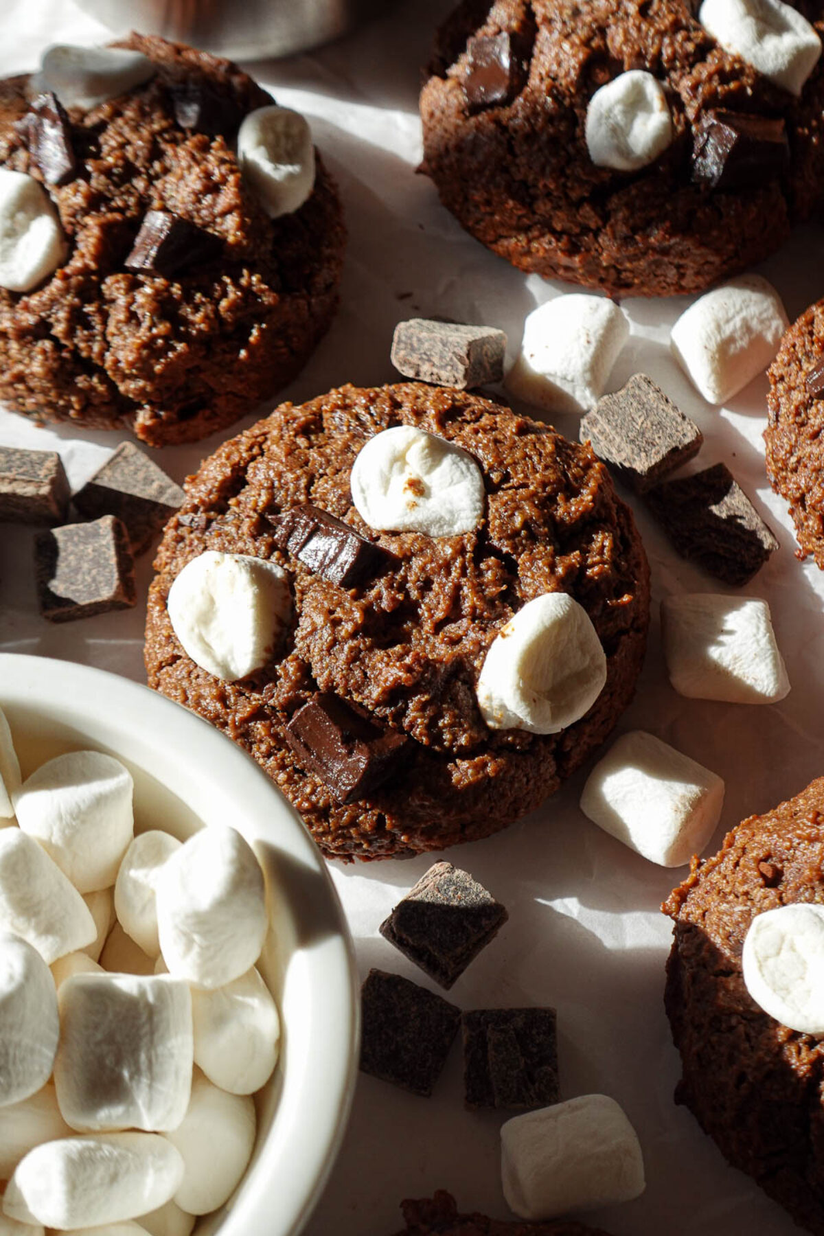 Close-up of a vegan and gluten-free hot chocolate cookie topped with chocolate chunks and marshmallows, highlighting its soft, chewy texture.