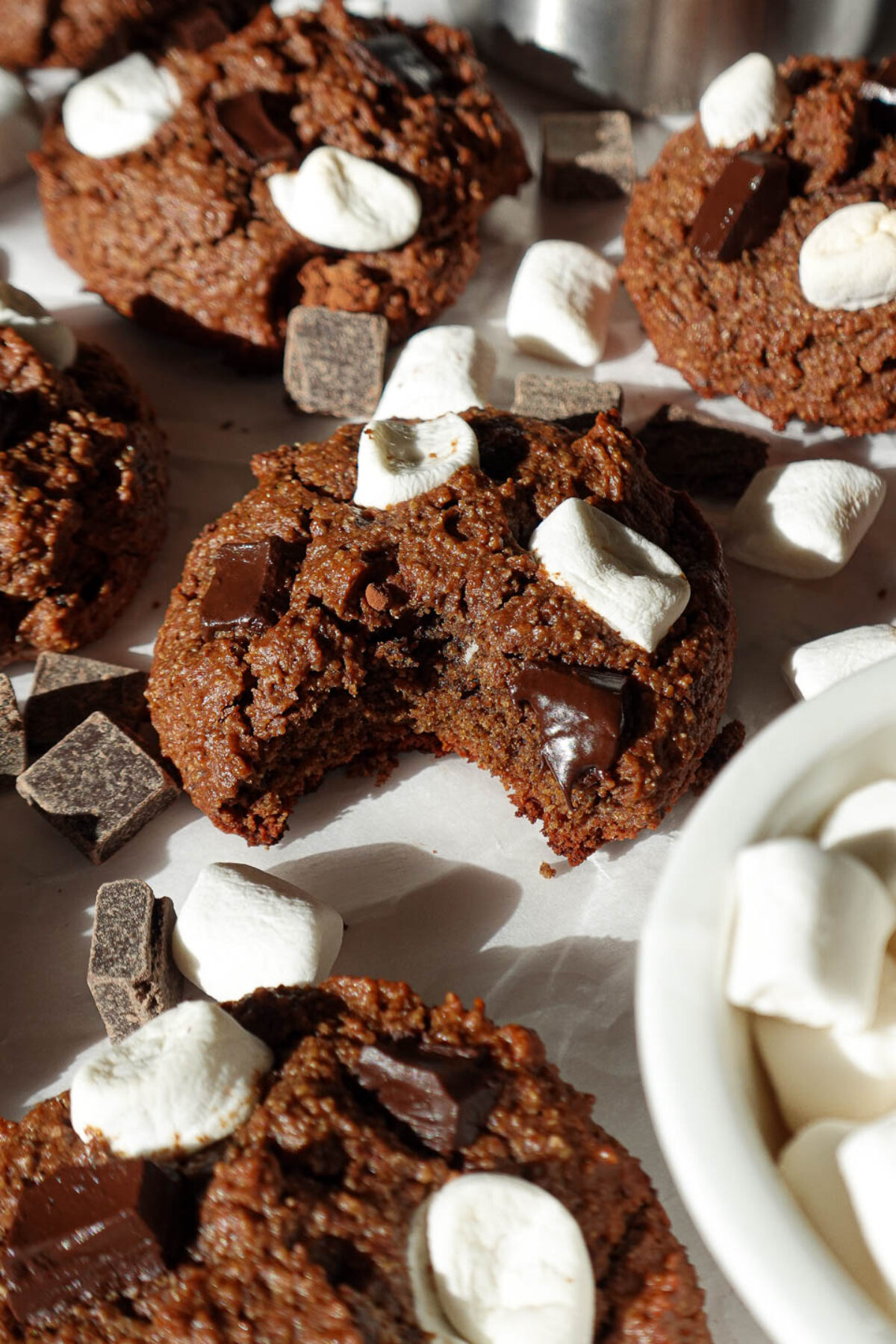 A vegan hot chocolate cookie with a bite taken out, showing a soft, chewy texture and gooey melted chocolate with mini marshmallows.