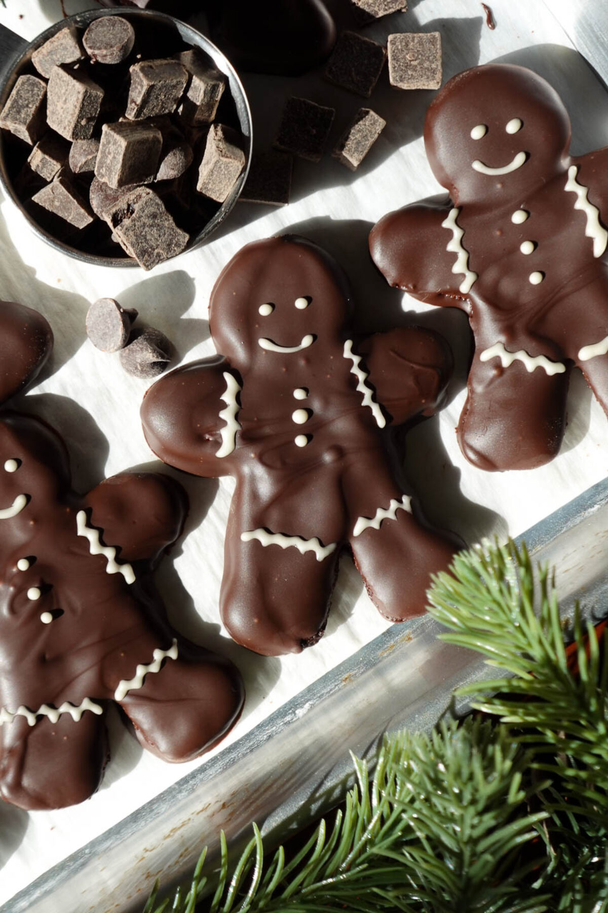 Festive vegan chocolate peppermint cookies in the shape of gingerbread men, coated in melted chocolate and adorned with white chocolate decorations