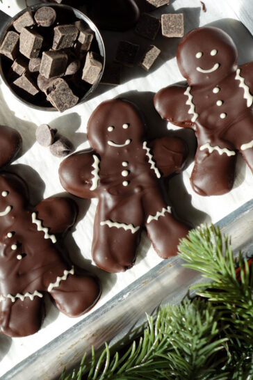 Festive vegan chocolate peppermint cookies in the shape of gingerbread men, coated in melted chocolate and adorned with white chocolate decorations