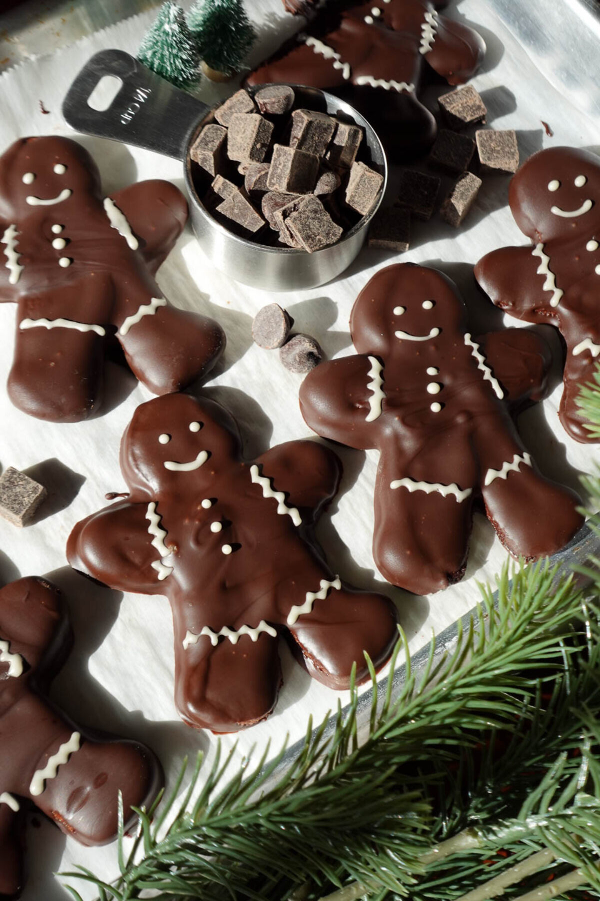Festive vegan chocolate peppermint cookies in the shape of gingerbread men, coated in melted chocolate and adorned with white chocolate decorations