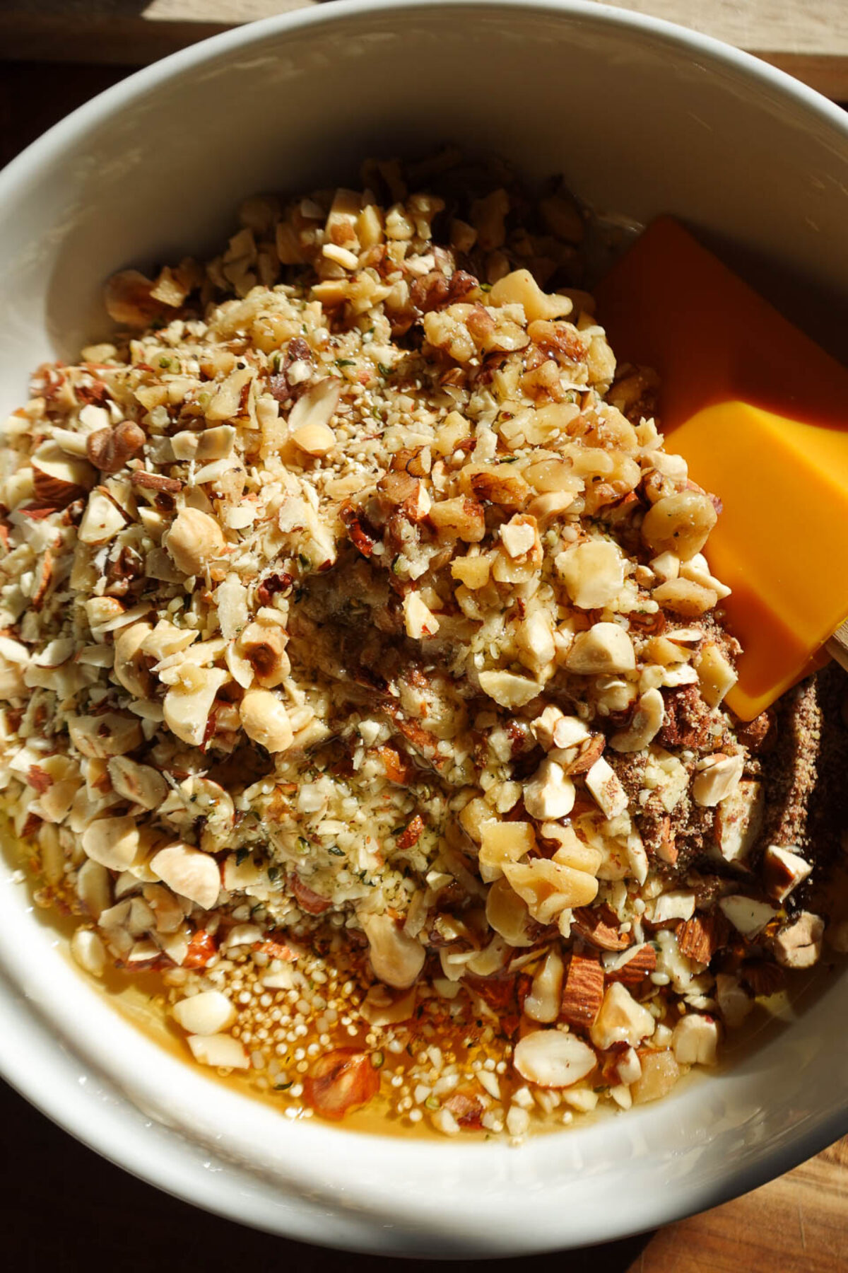 A large bowl filled with a mix of hazelnuts, almonds, pecans, chia seeds, hemp seeds, and maple syrup, ready to be stirred