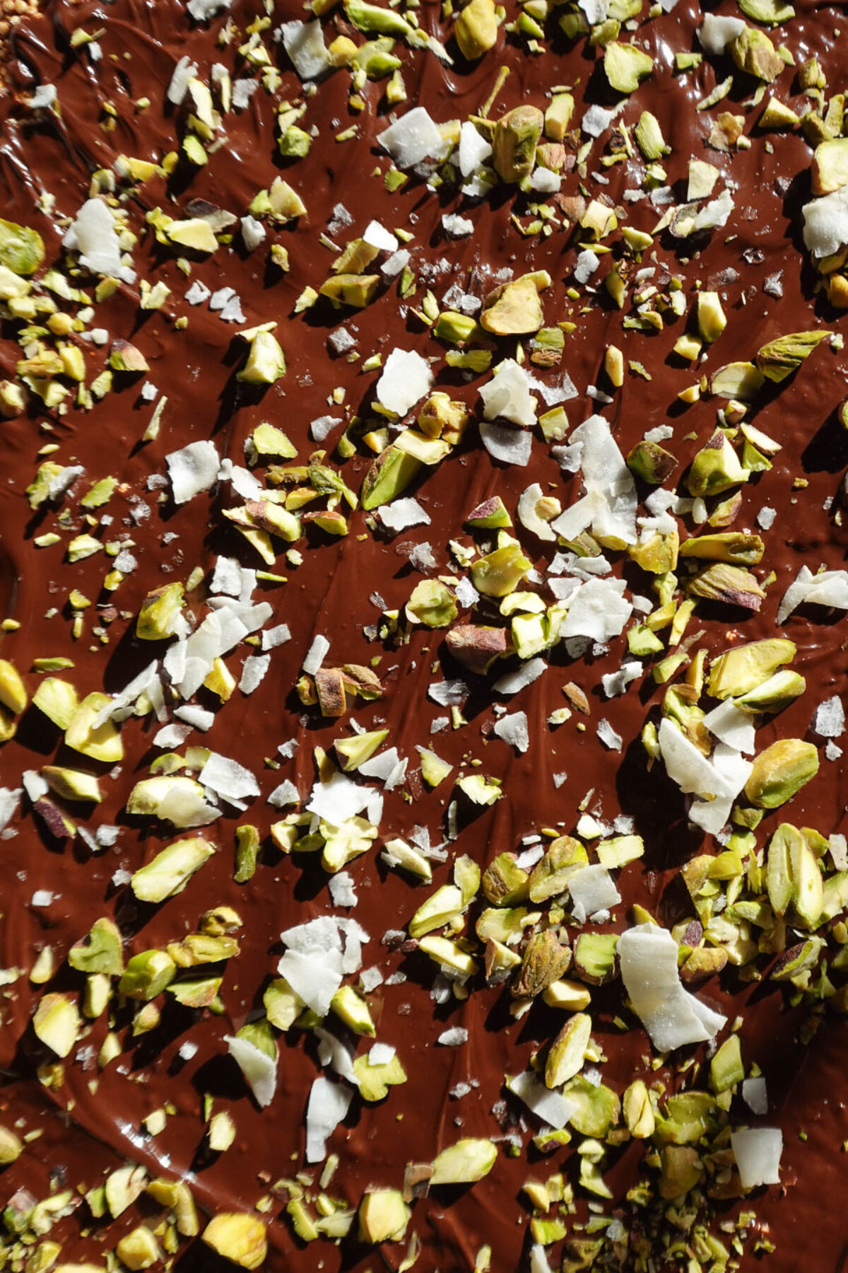 Bark topped with shredded coconut, chopped pistachios, and flaky sea salt, just before freezing