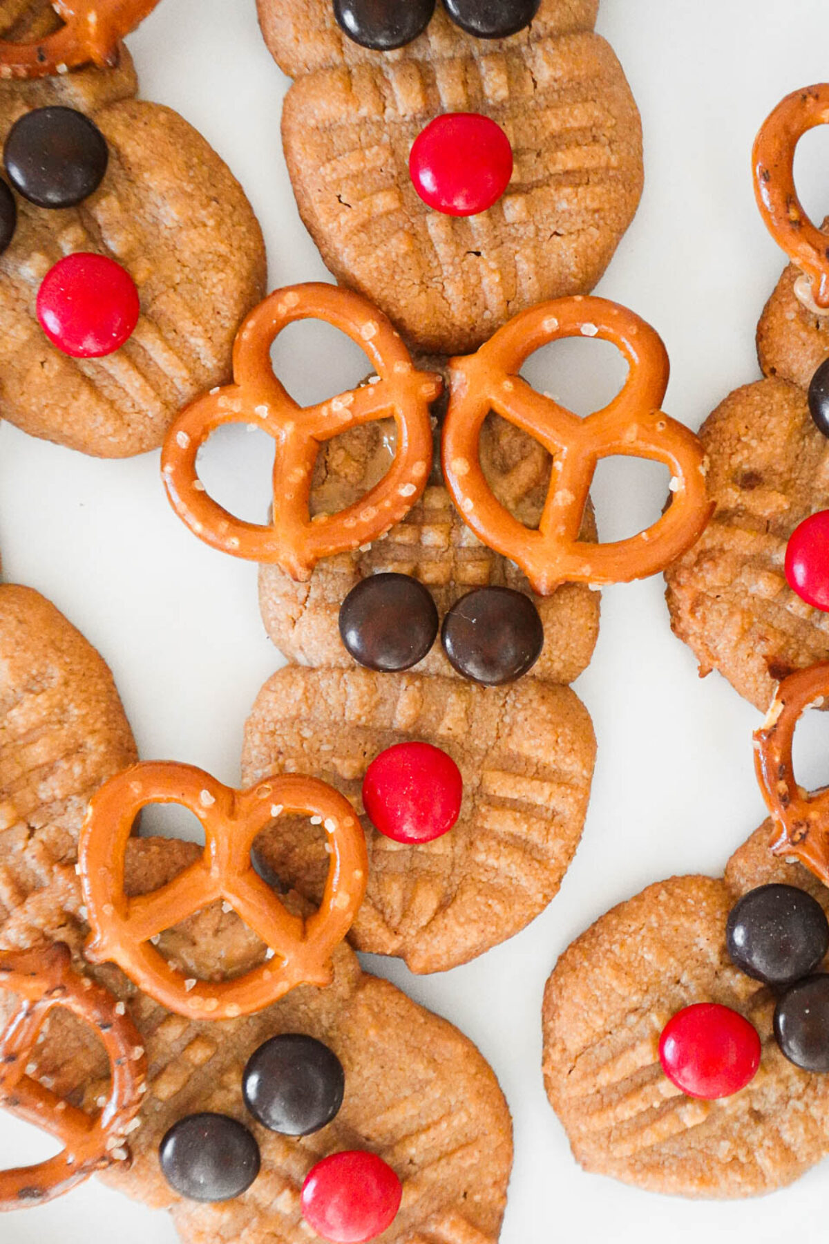 Close-up of vegan and gluten-free homemade Nutter Butter cookies decorated as reindeer with pretzel antlers, candy eyes, and a red candy nose.