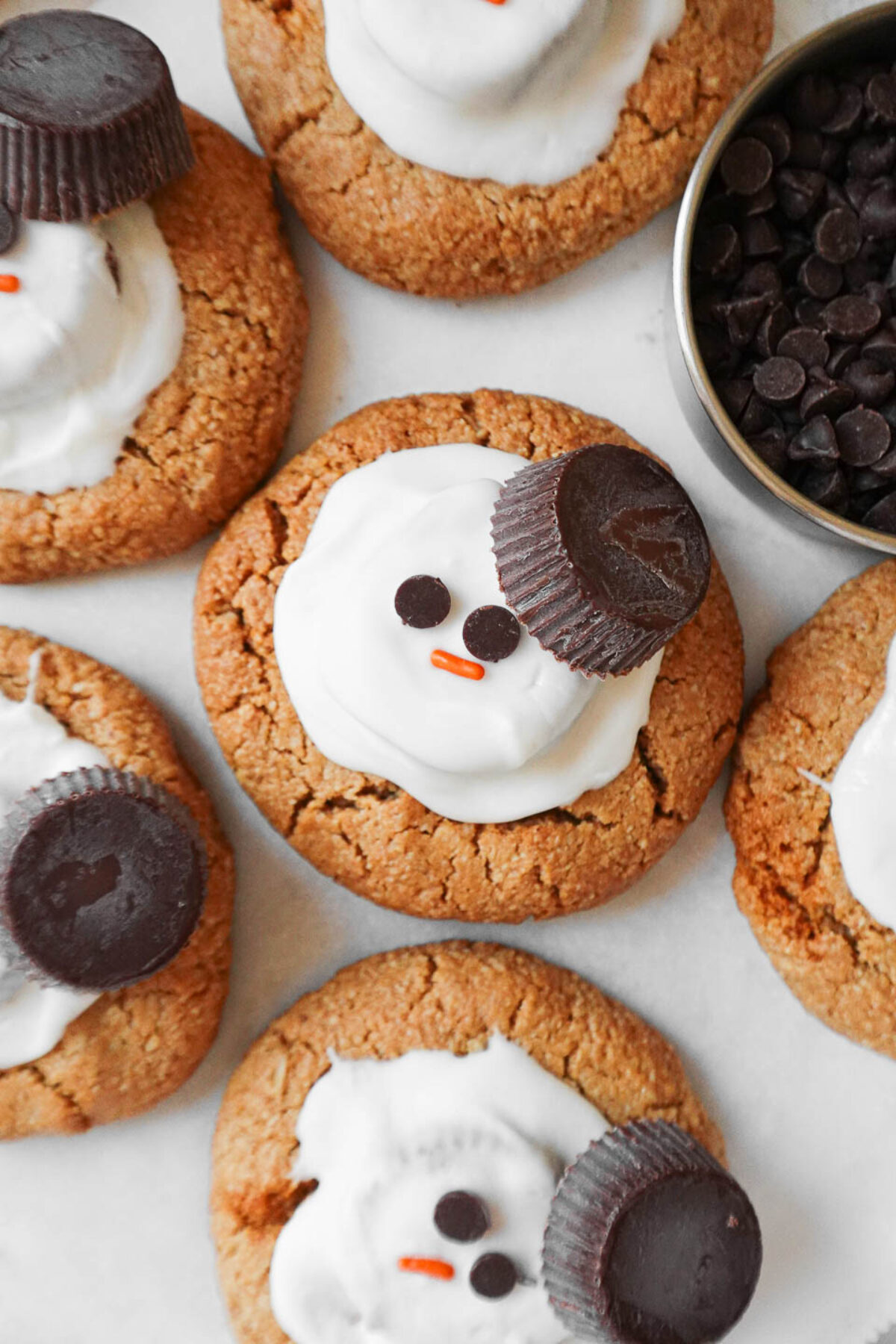 Vegan melted snowman peanut butter cookies decorated with white chocolate, peanut butter cups, and mini chocolate chips