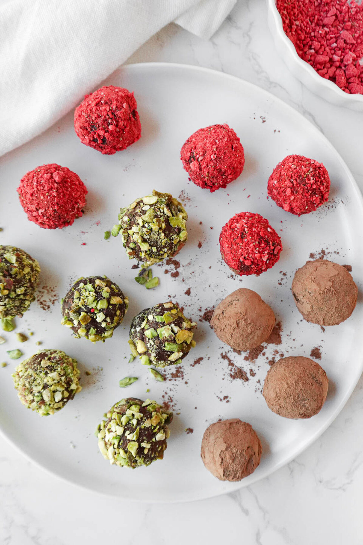 A plate of vegan chocolate avocado truffles coated in cocoa powder, crushed pistachios, and freeze-dried strawberry powder