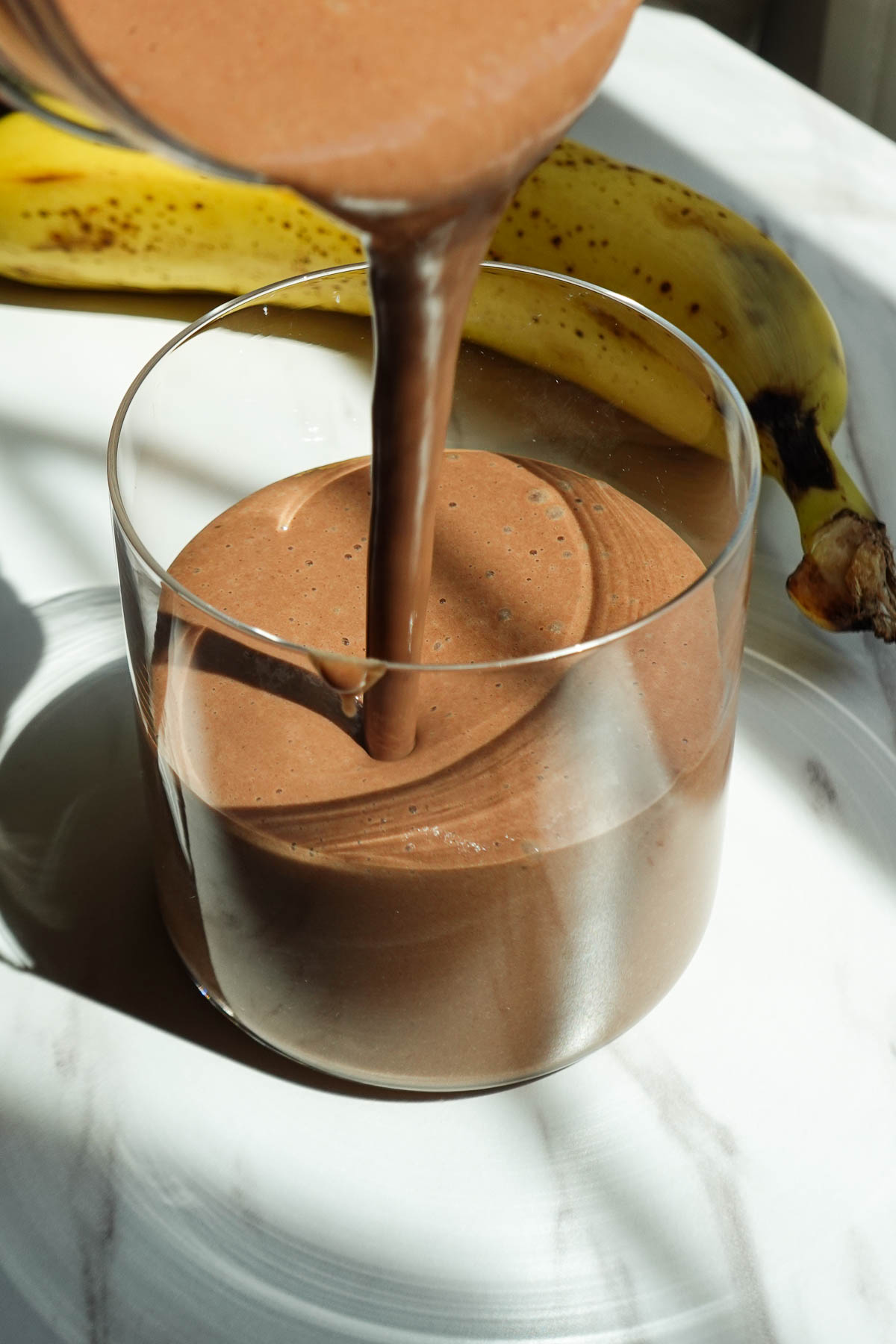 Pouring creamy chocolate peanut butter banana smoothie into a glass.
