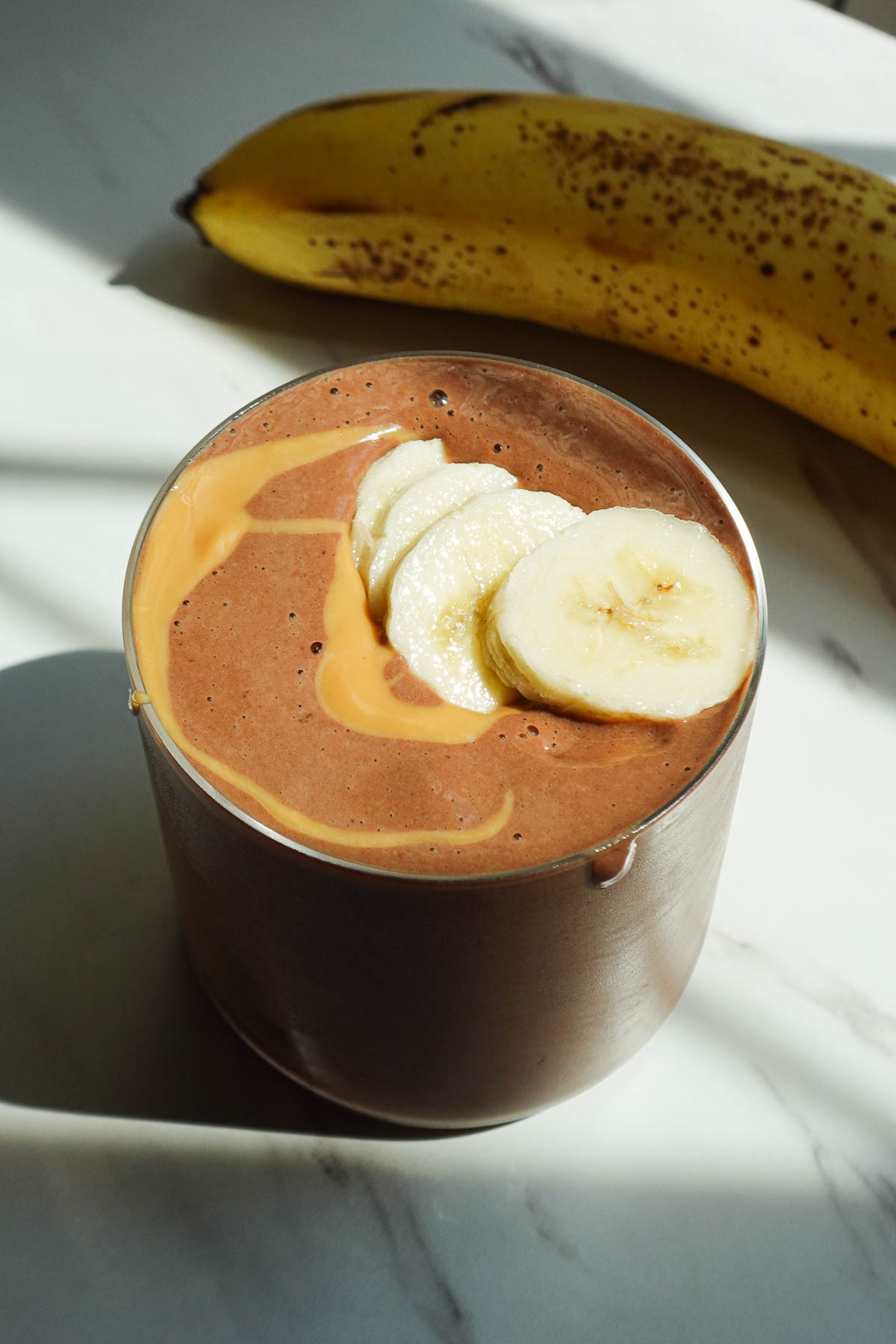 Chocolate peanut butter banana smoothie topped with banana slices and peanut butter.