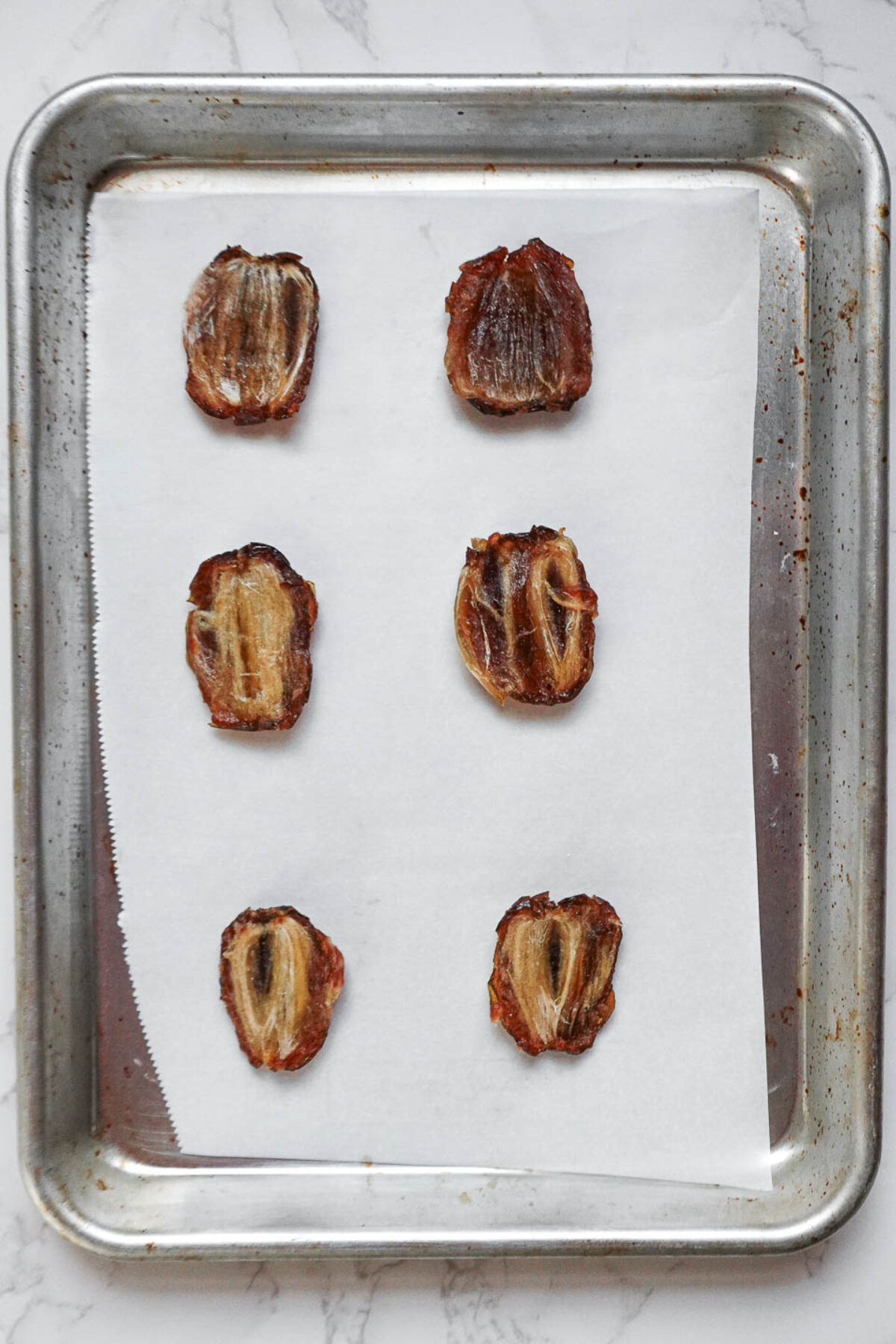 Sliced Medjool dates on a parchment-lined tray, ready for assembling chocolate turtles.