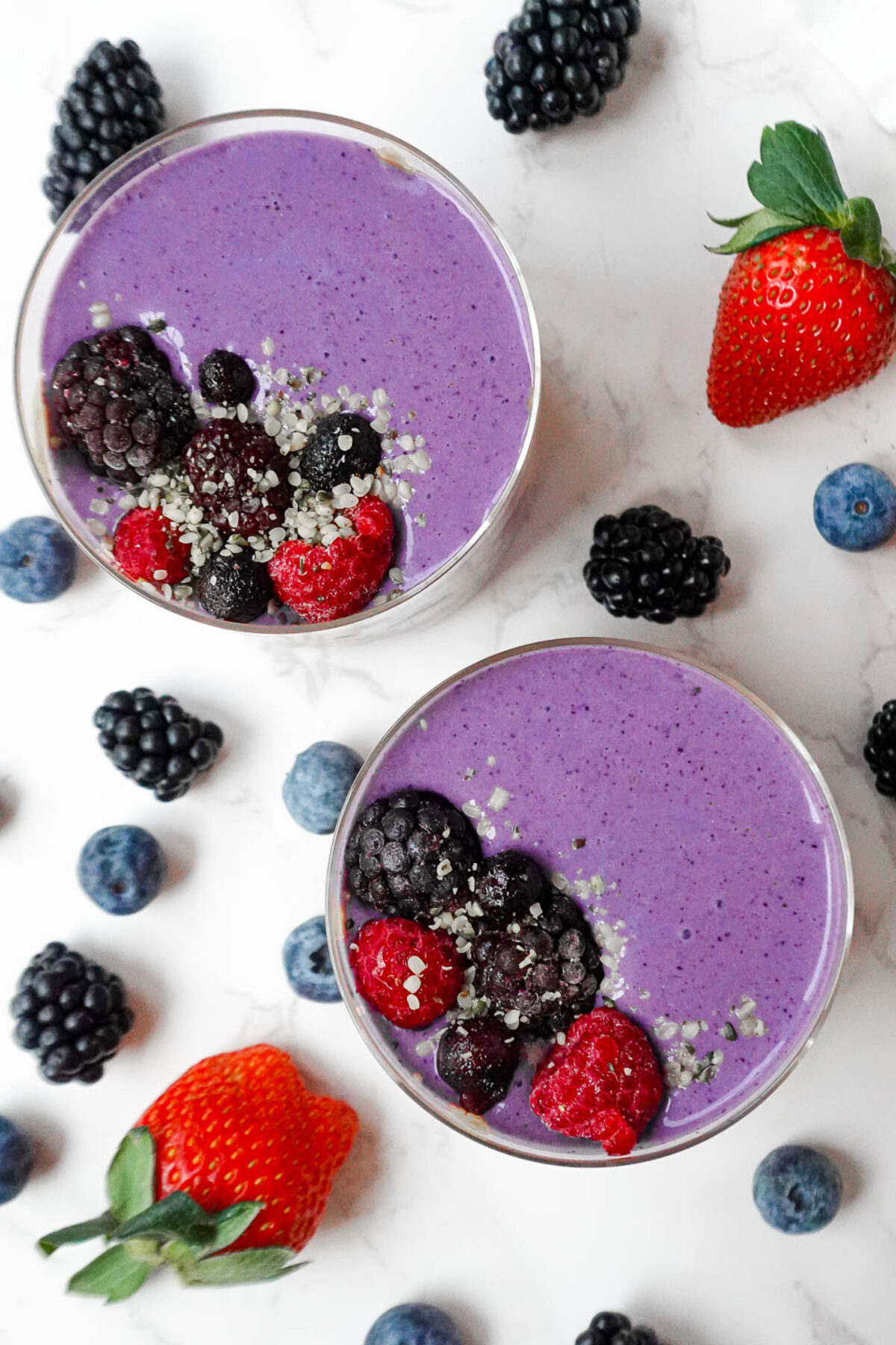 Peanut butter and jelly smoothie in a glass, topped with fresh berries, and marble table decorated with fresh berries
