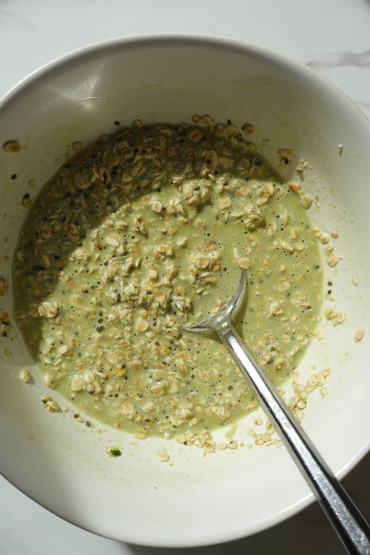 Mixing oats, chia seeds, non-dairy milk, maple syrup, matcha powder, vanilla extract, and pistachio butter to make pistachio overnight oats.
