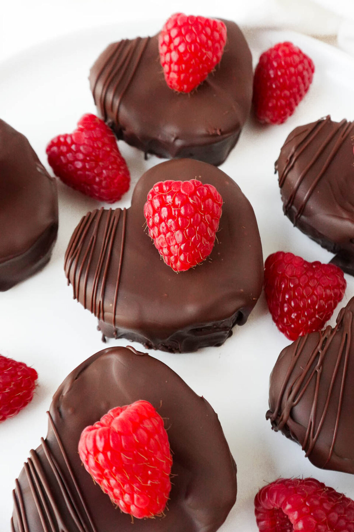 Close-up of a chocolate-coated brownie with a layer of raspberry jam inside, surrounded by raspberries and chocolate drizzle.